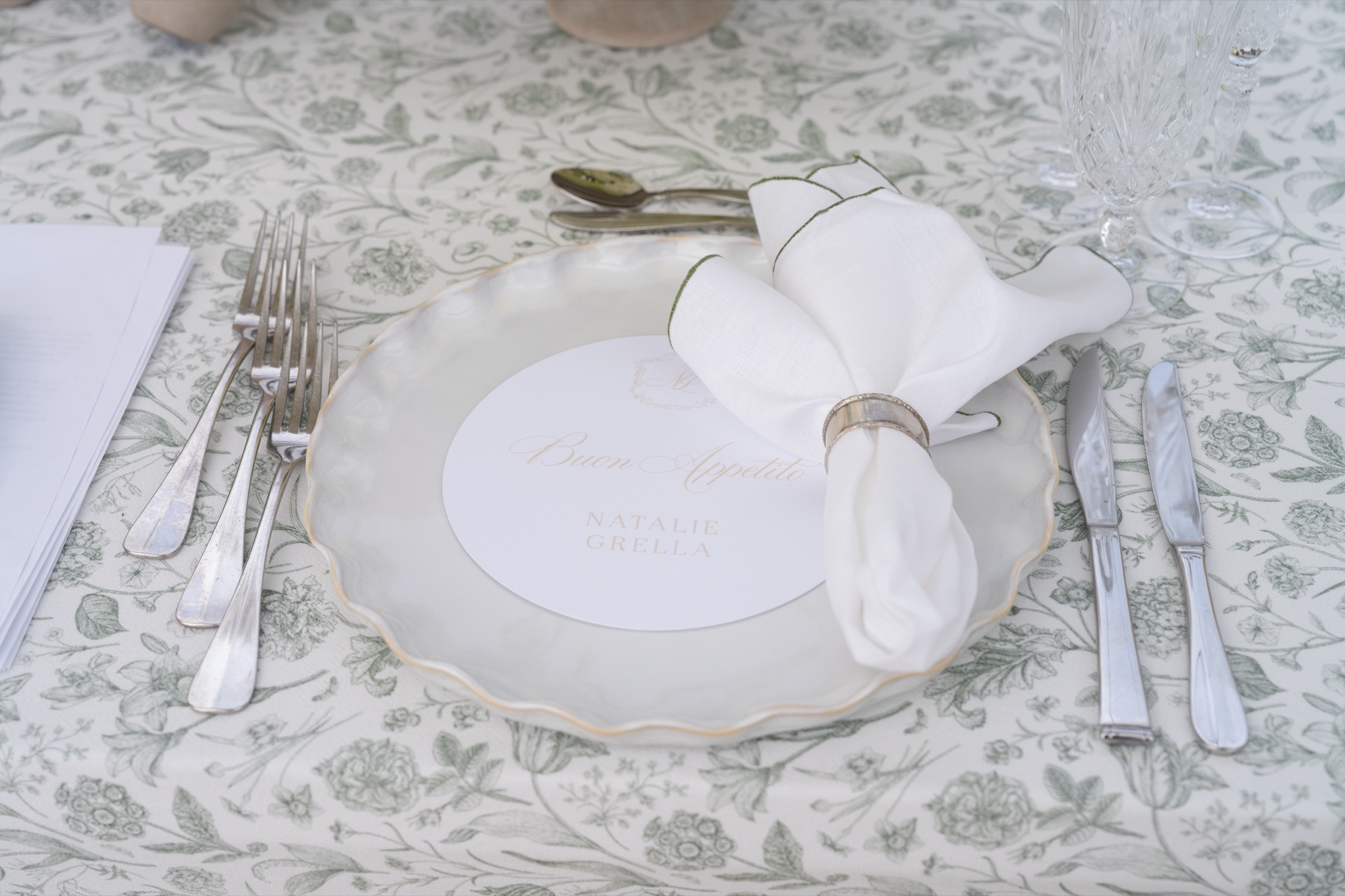 A place setting on green toile with a monogrammed menu and a folded napkin