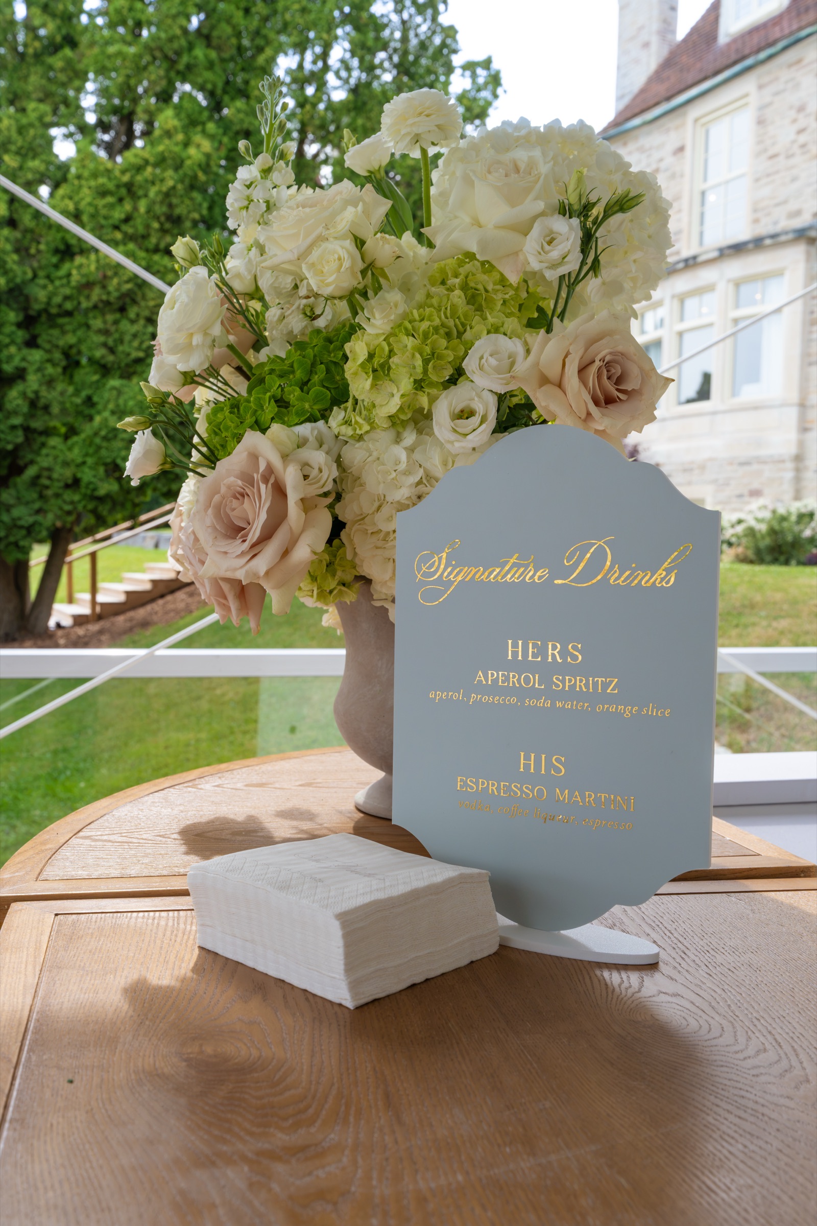 A signature drinks sign in pale blue beside blush roses and hydrangea