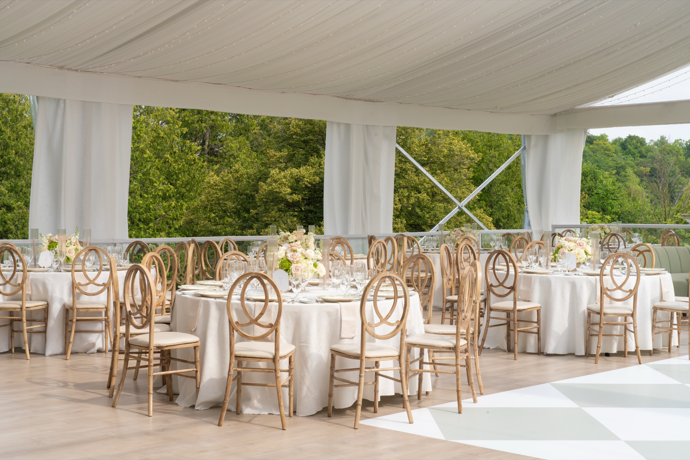 Round tables under the Eaton Hall tent with rattan chairs and the lawn beyond