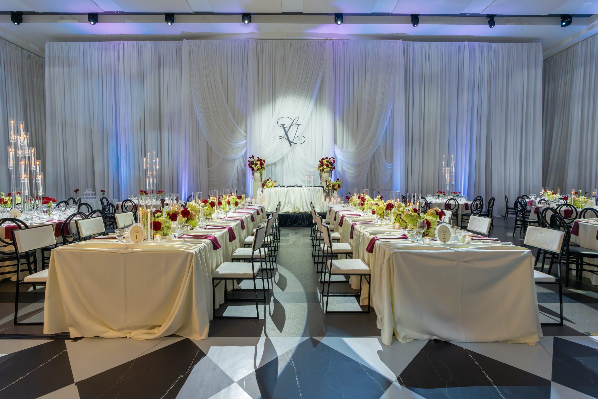The Paramount ballroom set for dinner, with ivory draping washed in violet light and a monogram lit on the far wall