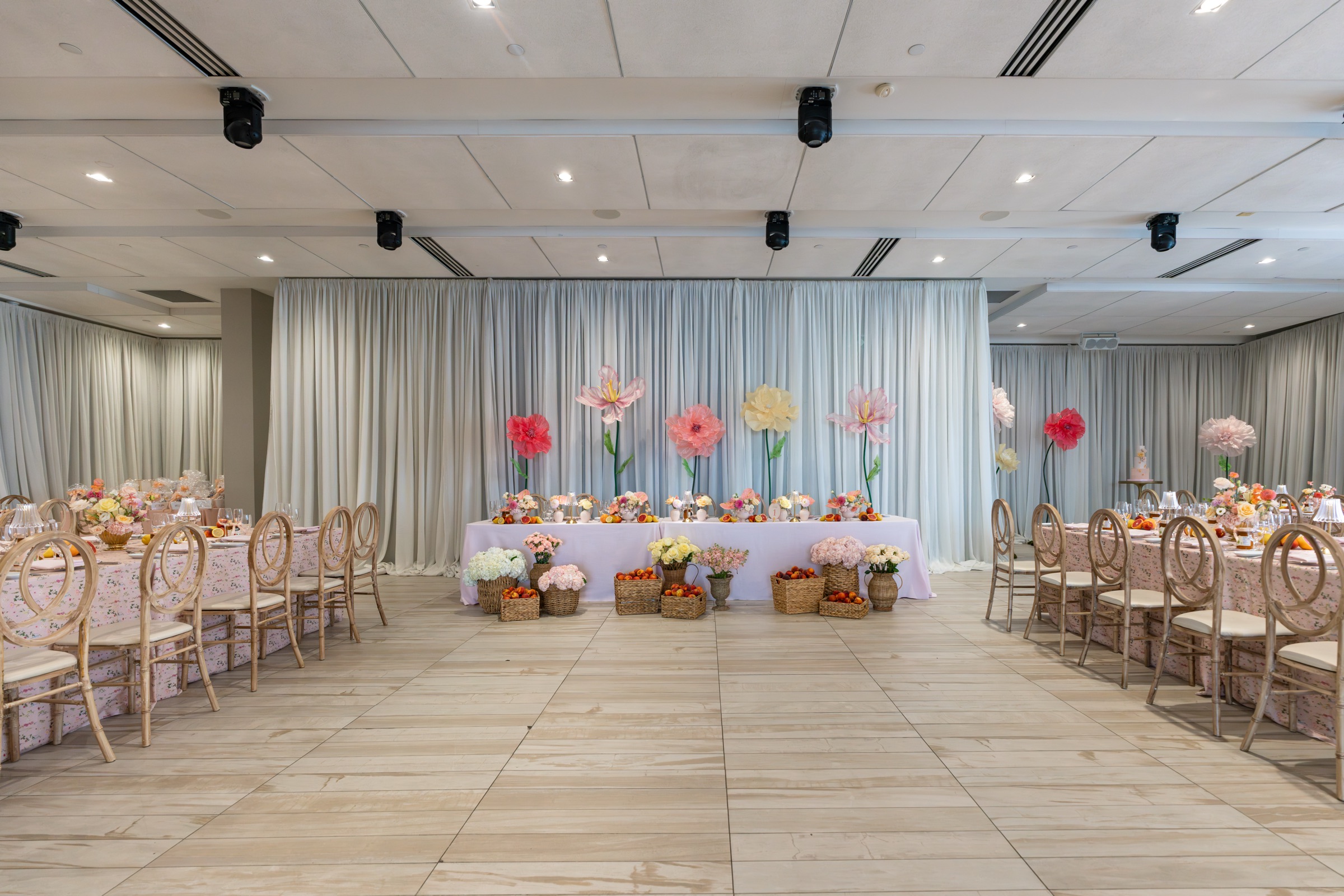 A long head table at Universal Eventspace under a row of giant paper flowers in coral, blush and yellow